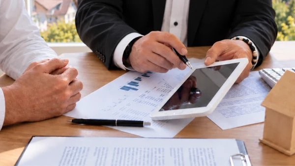 Ein Finanzberater erläutert einem Kunden anhand von Tablet und Unterlagen individuelle Finanzierungsmöglichkeiten für eine Baufinanzierung Bodensee.
