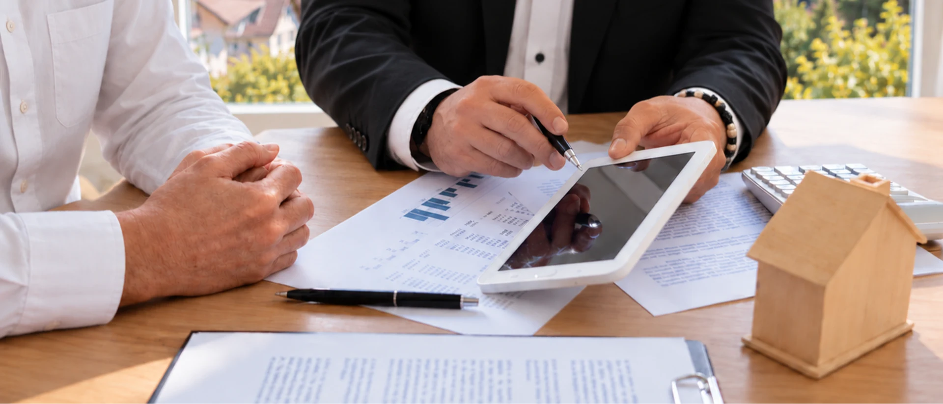 Ein Finanzberater erläutert einem Kunden am Tablet Finanzierungsunterlagen und Berechnungen zur individuellen Planung einer Baufinanzierung Bodensee.